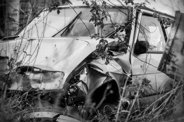 Photo of damaged and rusty car after crash, black and white.