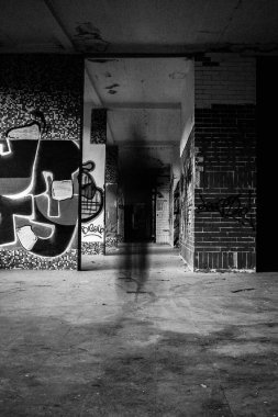 Karanlık bir koridorda yürüyen yalnız bir adamın hayaletli silueti, uzun pozlama. Karanlık korku konsepti, dramatik kara film sahnesi. Siyah ve beyaz görüntü, dikey çekim.