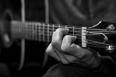 Adam akustik batı gitarı çalıyor. Parmaklarına odaklan, kapat. Siyah ve beyaz resim.