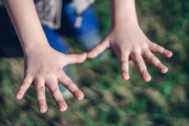Small child's outstretched dirty hands on the green grass background in the park. Hygiene concept, close up.