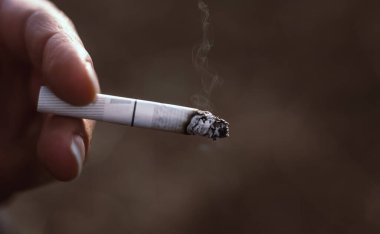 Man or woman holding a burning cigarette, unhealthy lifestyle concept. Bad habit, nicotine addiction, close up, copy space.