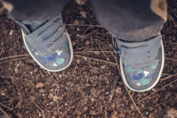 Little boy's dirty sneakers on the ground outdoors. Selective focus, view from above, top view.