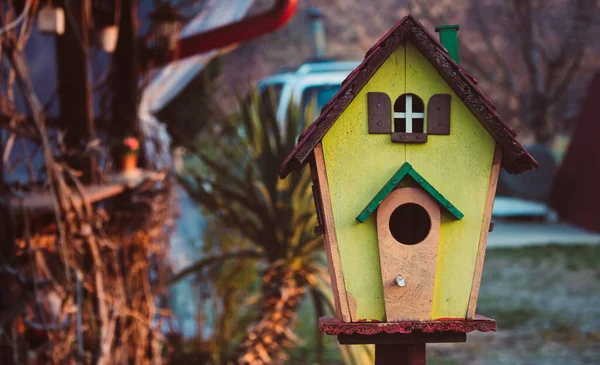 A small colorful wooden bird house outside in the garden.