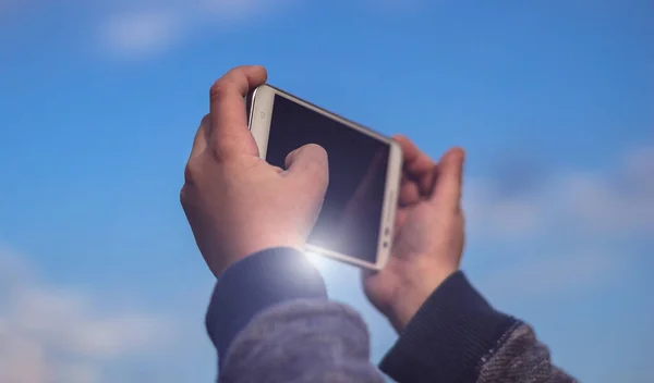 Little boy or a girl holding a smartphone using both hands and taking a photo of the blue sky. Travel concept, close up.