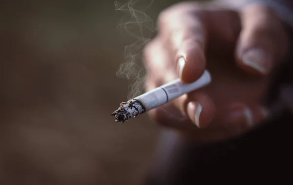 Woman holding a burning cigarette, unhealthy lifestyle concept. Bad habit, nicotine addiction, close up, copy space.
