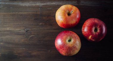 Three ripe organic red apples on the old brown wooden table. Top view, copy space.