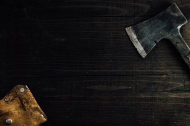 Old small dusty hunting axe with leather case. Top view, copy space, dark wooden background.