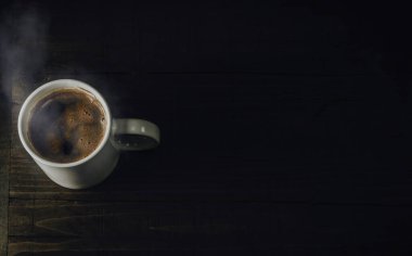 White mug full of hot beverage. Cup of steaming coffee on dark wooden table. Top view, copy space for text.
