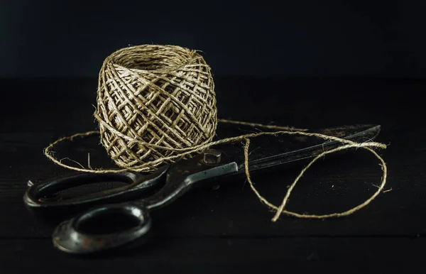 Old vintage rusty scissors with thread yarn twine ball. Wooden surface, dark tone, close up.