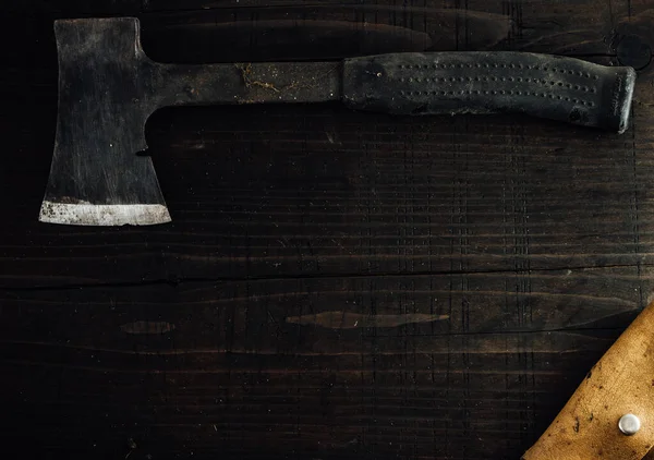 Old small dusty hunting axe with leather case. Top view, copy space, dark wooden background.