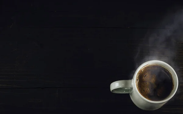 White mug full of hot beverage. Cup of steaming coffee in the corner of dark wooden table. Top view, copy space for your text.