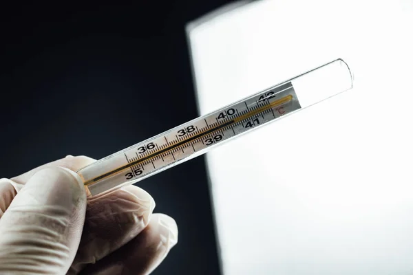 Close up of thermometer showing high temperature. Doctor wearing gloves holding a thermometer is a symbol of the fight against Corona virus Covid-19 outbreak. Medical healthcare and treatment concept.