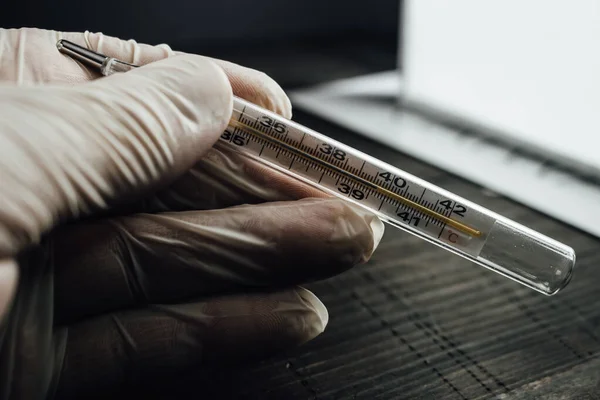 Close up of thermometer showing high temperature. Doctor wearing gloves holding a thermometer is a symbol of the fight against Corona virus Covid-19 outbreak. Medical healthcare and treatment concept.