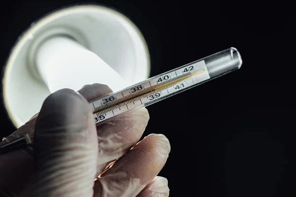 Doctor wearing rubber gloves holding a thermometer in his office. High body temperature is one of the symptom of new Covid-19 Corona virus. Close up, medical healthcare, disease treatment concept.