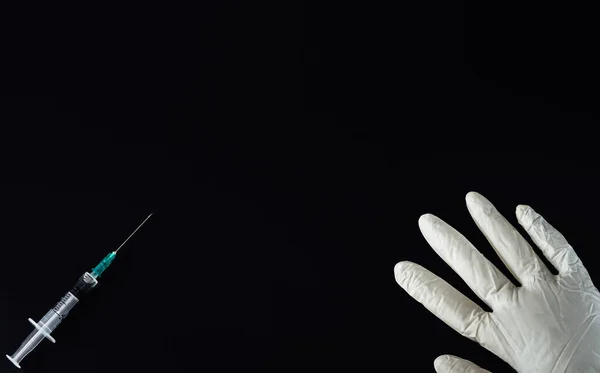 Isolated medical equipment on black background. Rubber glove and syringe with attached needle. Medical health care concept, top view, copy space.