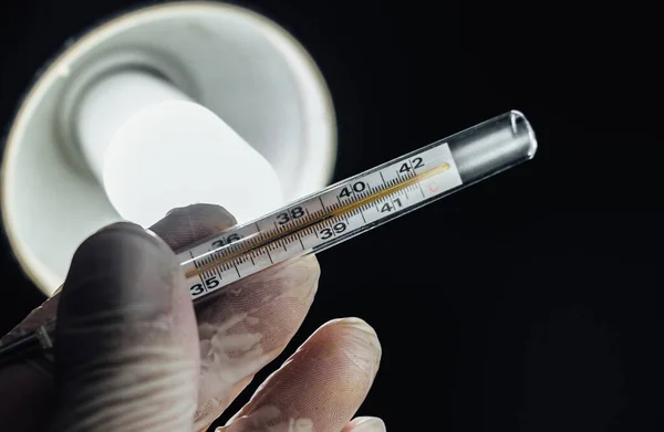 Doctor wearing rubber gloves holding a thermometer in his office. High body temperature is one of the symptom of new Covid-19 Corona virus. Close up, medical healthcare, disease treatment concept.