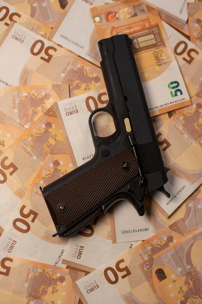 Bir tabanca büyük bir banknot yığını üzerine yerleştirilir ve tüm resmi kapsar.