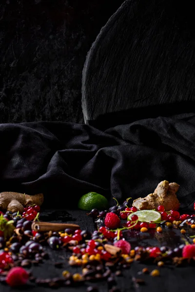 Black background of wood, metal and fabric with cinnamon, ginger, lime, raspberries, red currants, black currants, coffee beans