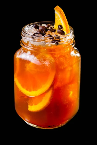 Orange, grapefruit and coffee syrup lemonade in a glass jar with ice. On top is a slice of orange and coffee beans. Black background.