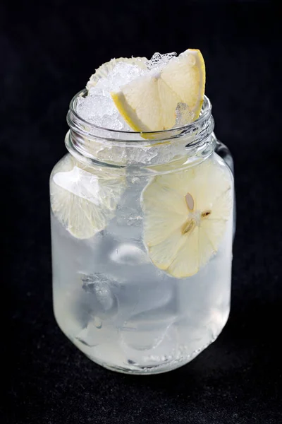 Tonic with lemon, sugar syrup and ice. Drink in a transparent jar. Black background