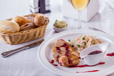 Kırmızı, tatlı soslu kızarmış tavuk filetosu, pilav, bir sepet ekmek ve beyaz yuvarlak tabakta bir bardak beyaz şarap. Yatay yönelim