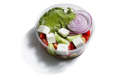 Mozzarella with cucumbers, tomatoes, onions and pesto sauce in a plastic container on a white plate