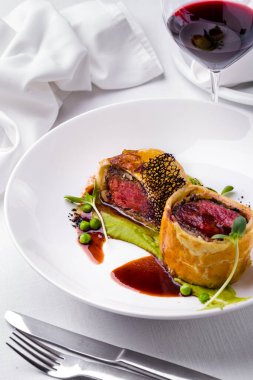 Ekmek kabuklu kızarmış et, bezelye sosu, yeşil bezelye, beyaz tabakta sığır eti salatası ve bir bardak şarap. Dikey yönelim