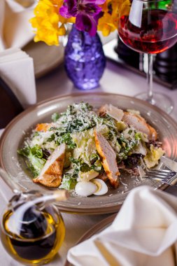 Salad with meat, boiled egg, cheese, salad, arugula in a plate on the table with olive oil and a glass of wine