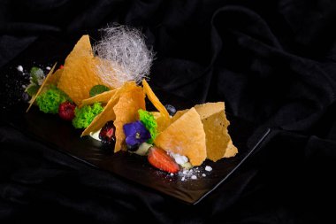 Ice cream with chips, blackberries, blueberries, raspberry icing sugar and sugar threads on a black plate and a dark background. Horizontal orientation
