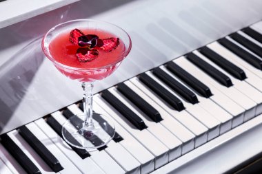Kurutulmuş çilekli kokteyl ve piyano klavyesinin üzerinde duran cam bir çiçek yaprağı.