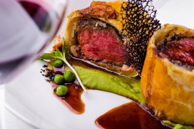 Ekmek kabuklu kızarmış et, bezelye sosu, yeşil bezelye, beyaz tabakta sığır eti salatası ve bir bardak şarap. Yatay yönelim