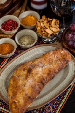 Oval tabakta Kubdari, üzümler, kurutulmuş elmalar, baharatlar, bir bardak kırmızı şarap. Dikey yönelim 