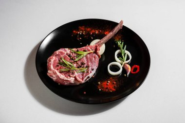 Raw pork meat on the bone with peas, paprika, chili, salt, rosemary, onions, garlic in a plate on a white background