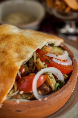 Domates, kabak, soğan, patlıcan ve hamur kapağıyla pişirilmiş havuç. Sebzeler odun ateşinde pişiriliyor. Tencere seramik tabakta. Yakınlarda, Gürcistan baharatlı seramik kaseler, bir bardak kırmızı şarap ve metal kâse wi var.