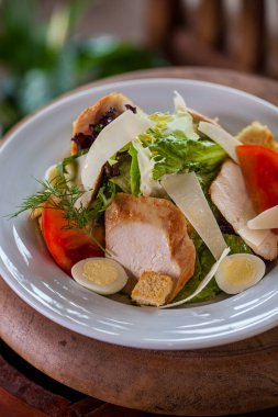 Salad with ham, endive, dill tomatoes, croutons, lettuce, cheese, in a plate on a wooden background