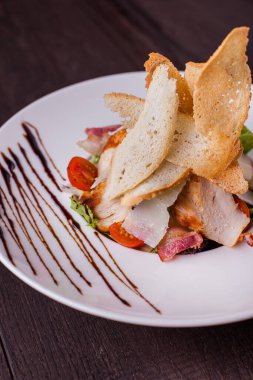 Salad with meat, bacon, tomatoes, cheese and bread in a plate on a wooden background