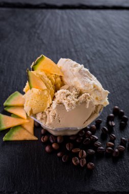 Vanilla ice cream scoops with melon pieces and chipped coffee beans on a stone background. Vertical orientation