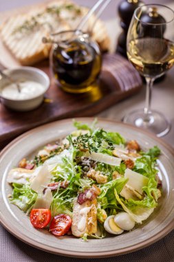 Salad with meat, tomatoes, lettuce, croutons, thyme, endive, boiled egg and mayonase in a plate on a light background with a glass of wine with cutlery