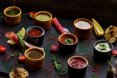 Doğu ve Kafkas mutfağı için sekiz farklı sos çeşitlendirdim. Soslar seramik sosların içinde. Uçan daireler siyah tahtada. Yanında prosciutto, vişneli domates, ızgara sarımsak, kapari, roka yaprağı, bir dilim limon ve baharat var.