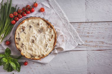 Cheese casserole with tomatoes, basil, onions and parsley on a towel lying on the table