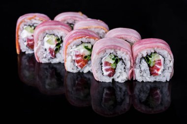 Roll with tuna, cucumber, pepper, onion, rice, nori and Philadelphia cheese on a black mirror background