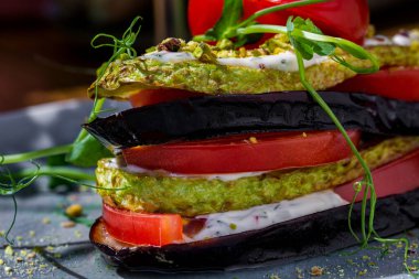 Eggplant, zucchini, tomatoes, pea sprouts, white sauce, pistachios in a plate on a wooden table