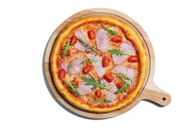Pizza with cheese, arugula, tomatoes, ham and sauce on a wooden board on a white plate
