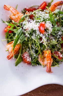 Karidesli salata, muz yaprağı, peynir, domates, roka, ahşap zemin üzerinde salata.