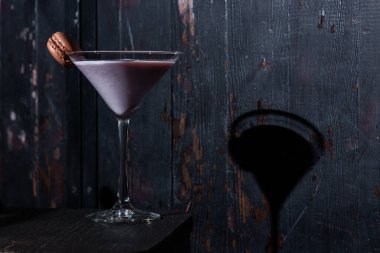 Milkshake with macaroni in a glass that stands on the table against the background of a dark green wall