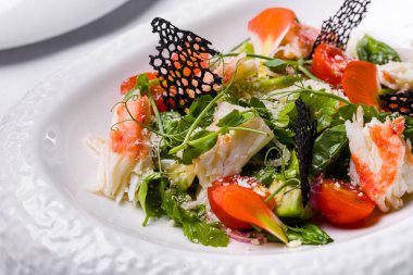 Yengeç salatası, bezelye filizi, domates, marul, dantel cips, maydanoz ve peynir tabakta.