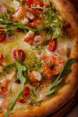 Pizza with cherry tomatoes, shrimps, arugula and cheese on a wooden board on the table