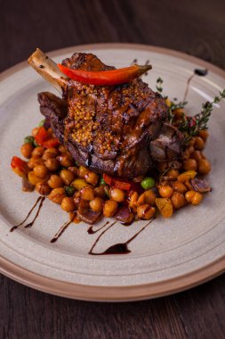 Kemiğin üzerinde kuzu kuzu eti, kekik, biber ve nohut ile ahşap bir arka planda bir tabak. Dikey yönelim