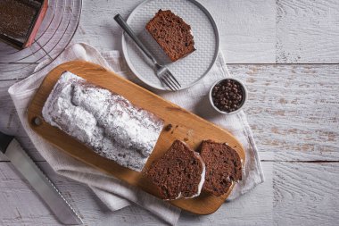 Chocolate bread sliced with candied fruit and chocolate on a wooden board with a towel and a knife on the table