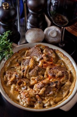 Kızarmış et parçaları, erimiş peynirli mantarlı kekik, yuvarlak tabakta çatal bıçak ve bir bardak şarapla. Dikey yönelim